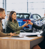 Young couple talking to a sales person in a car showroom
