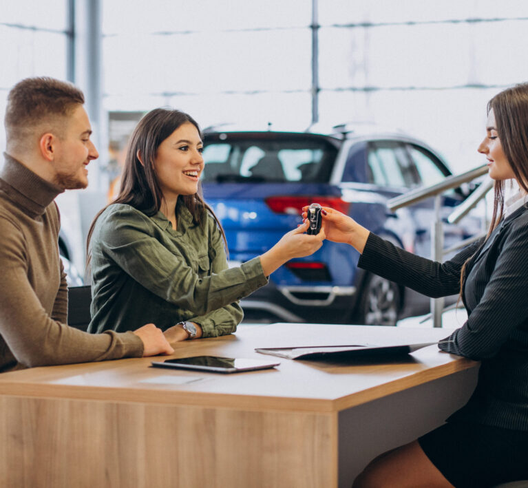 Young couple talking to a sales person in a car showroom